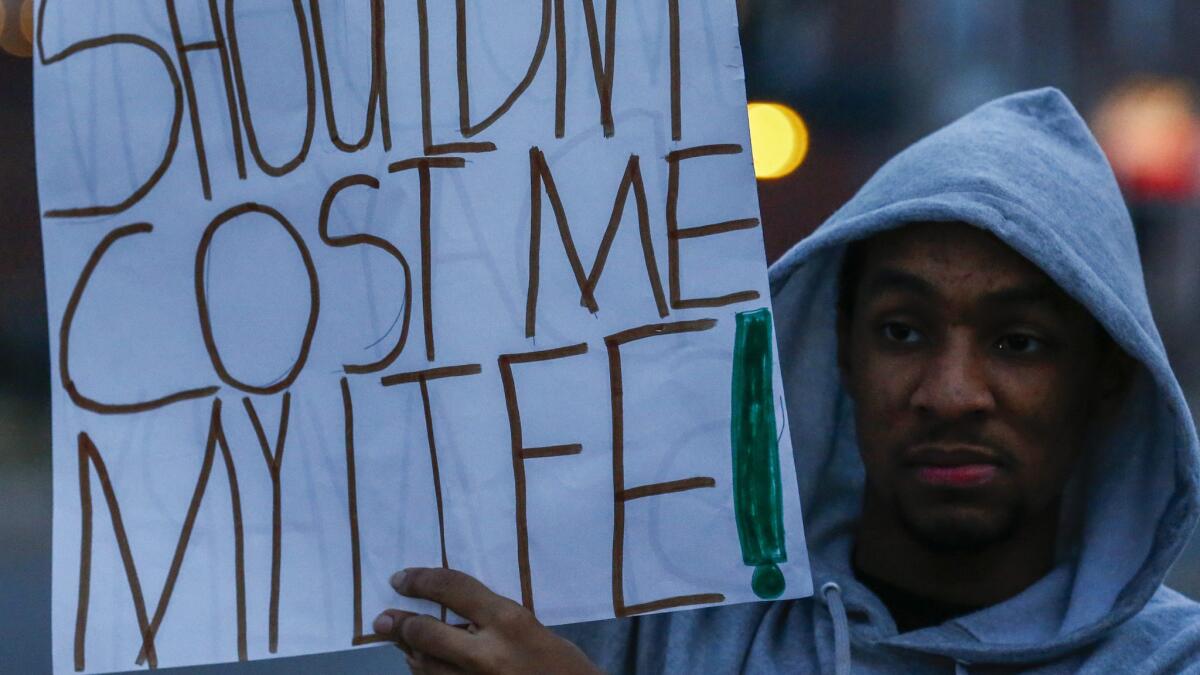 A protester holds a sign sayin, "My Hood Shouldn't Cost Me My Life," across the street from the Ferguson Police Department on Thursday evening.