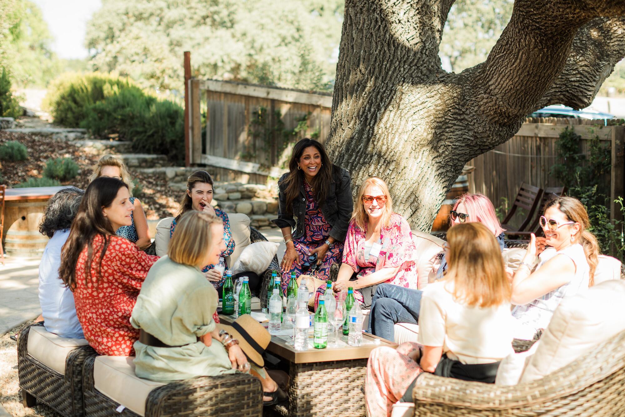 A broup of women eating and drinking under a live oak tree.