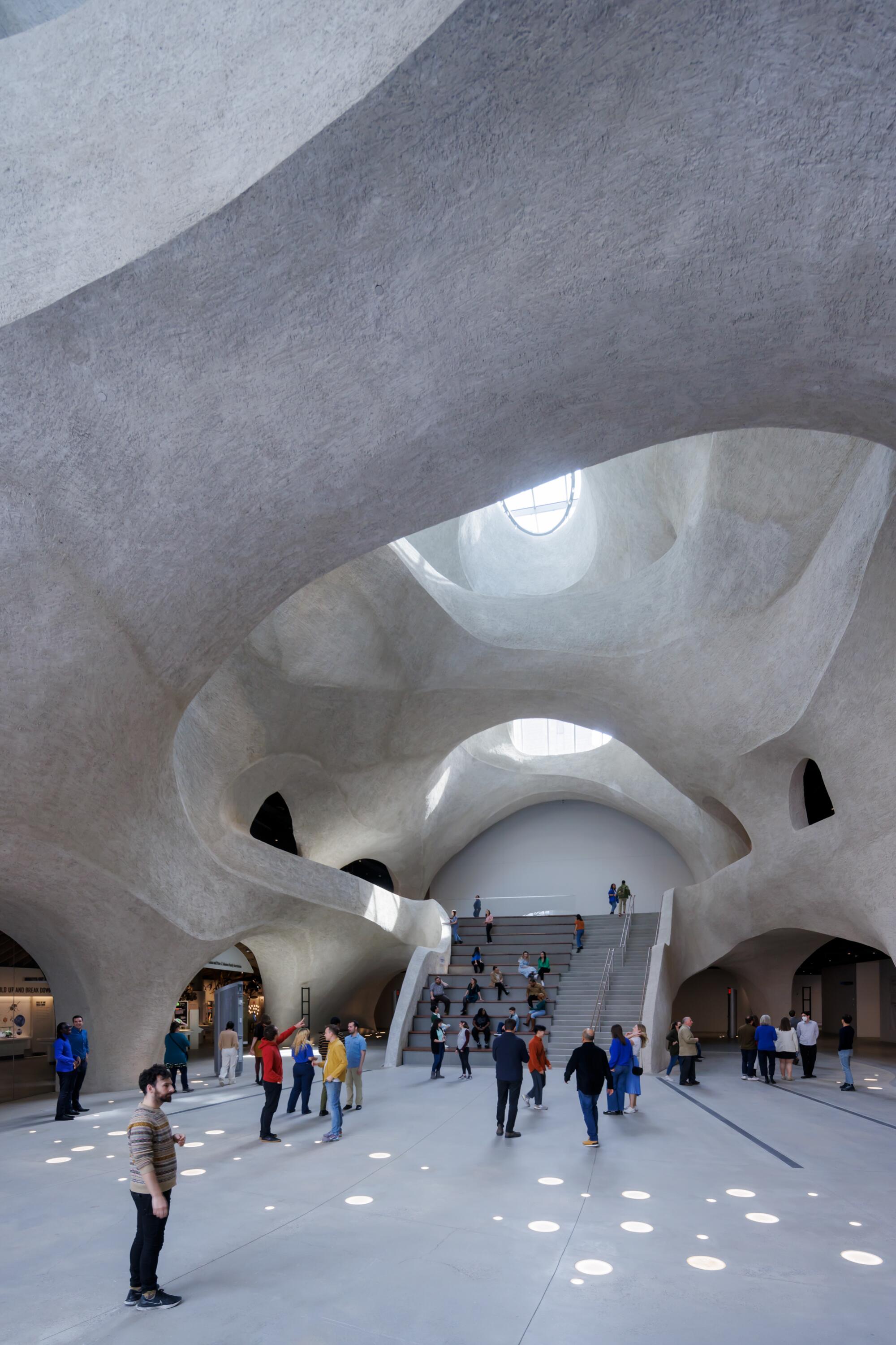 An atrium built to resumble a cave features a stepped seating area where visitors, including many children gather.