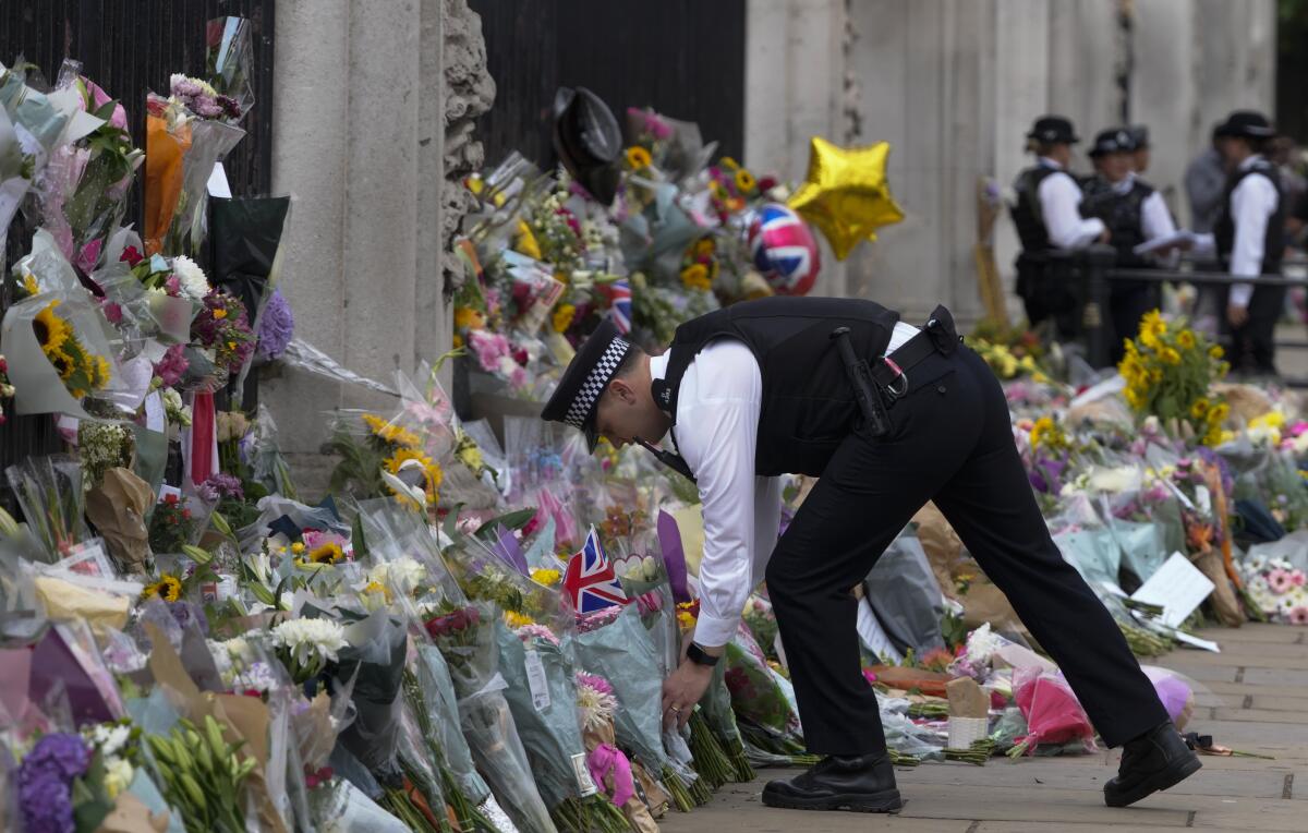 A police officers puts flowers brought by mourners at the gate of Buckingham Palace in London, Friday, Sept. 9, 2022. Queen Elizabeth II, Britain's longest-reigning monarch and a rock of stability across much of a turbulent century, died Thursday Sept. 8, 2022, after 70 years on the throne. She was 96. (AP Photo/Kirsty Wigglesworth)