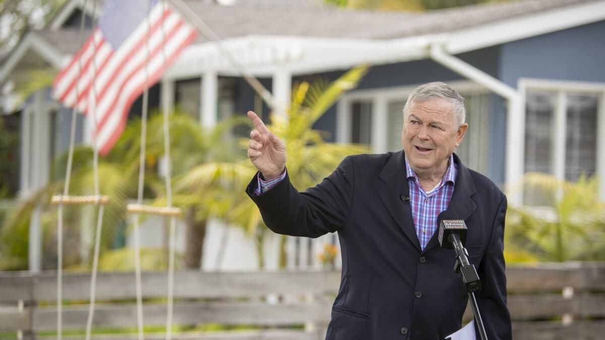 U.S. Rep. Dana Rohrabacher (R-Costa Mesa) points to a commercial aircraft that could be heard leaving nearby John Wayne Airport during a news conference at his home Monday.