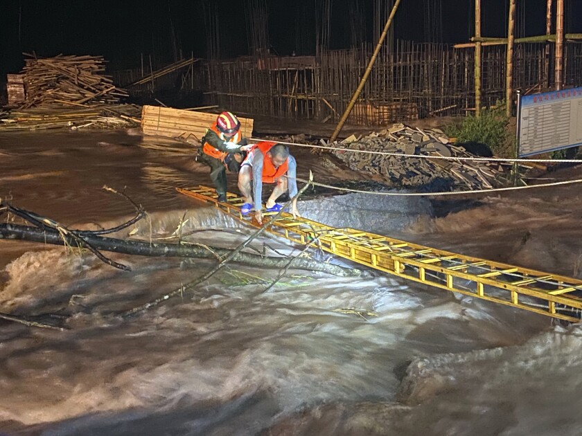 A rescuer helps a worker cross a ladder to get across floodwaters from a construction site in Jing'an county in central China's Jiangxi province midnight Friday, July 3, 2020. A wide swath of southern China braced Sunday for more seasonal rains and flooding. (Chinatopix via AP)