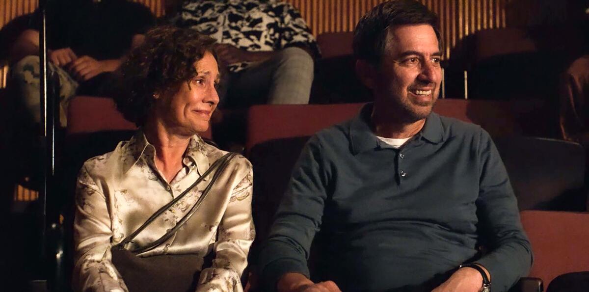 A woman and a man seated in a theater, looking to one side and smiling