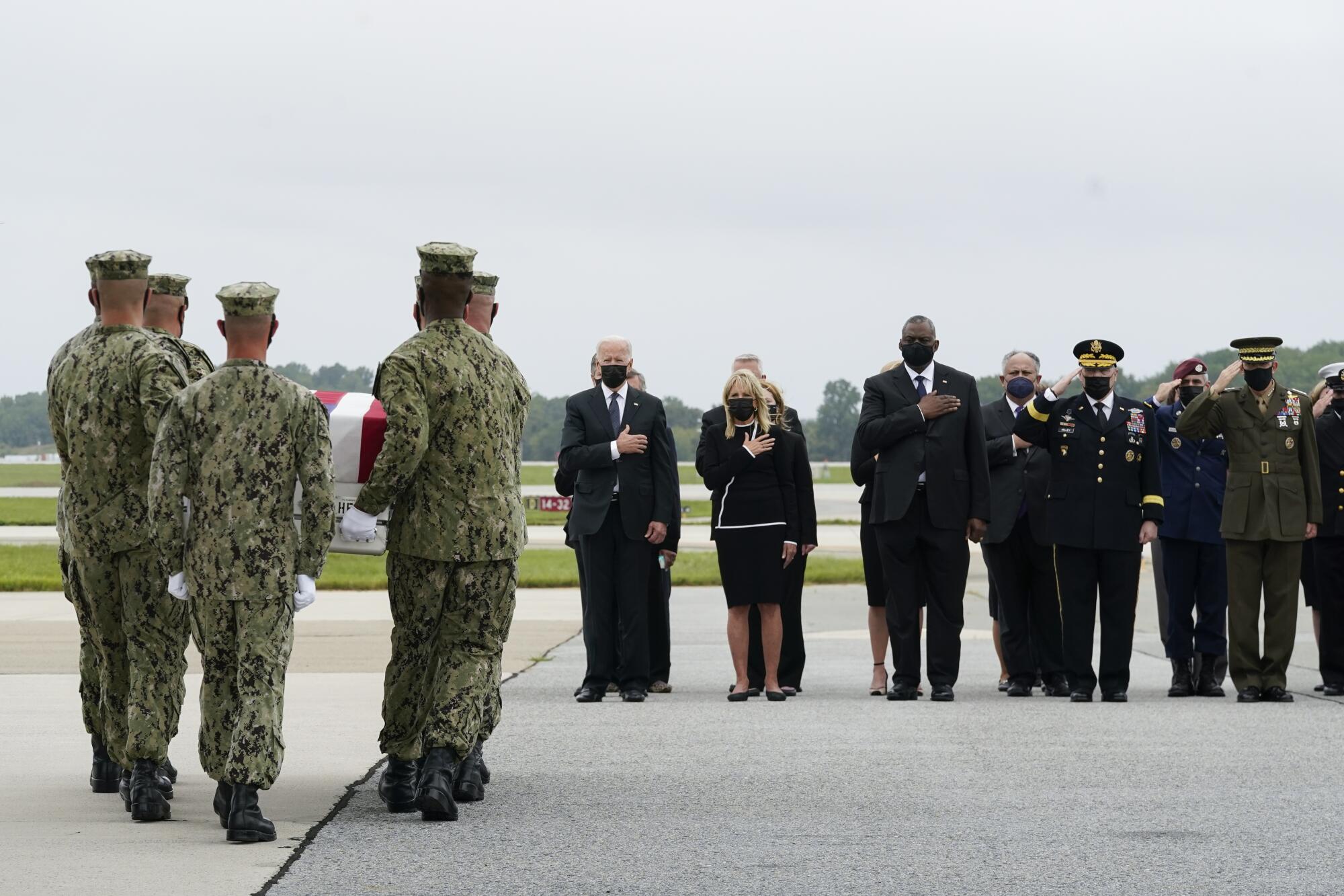 President Biden and others watch as a team carries a fallen service member's remains.