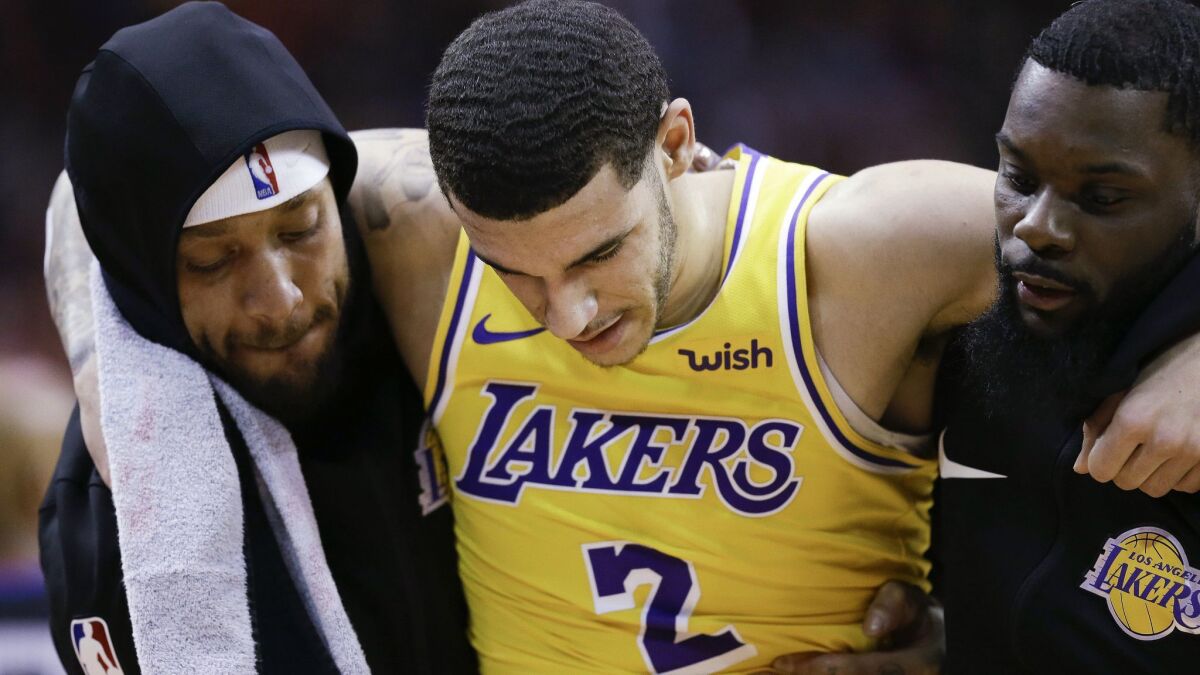 Lakers guard Lonzo Ball is carried off the court by Michael Beasley, left, and Lance Stephenson after Ball sustained an injury during the second half Saturday.