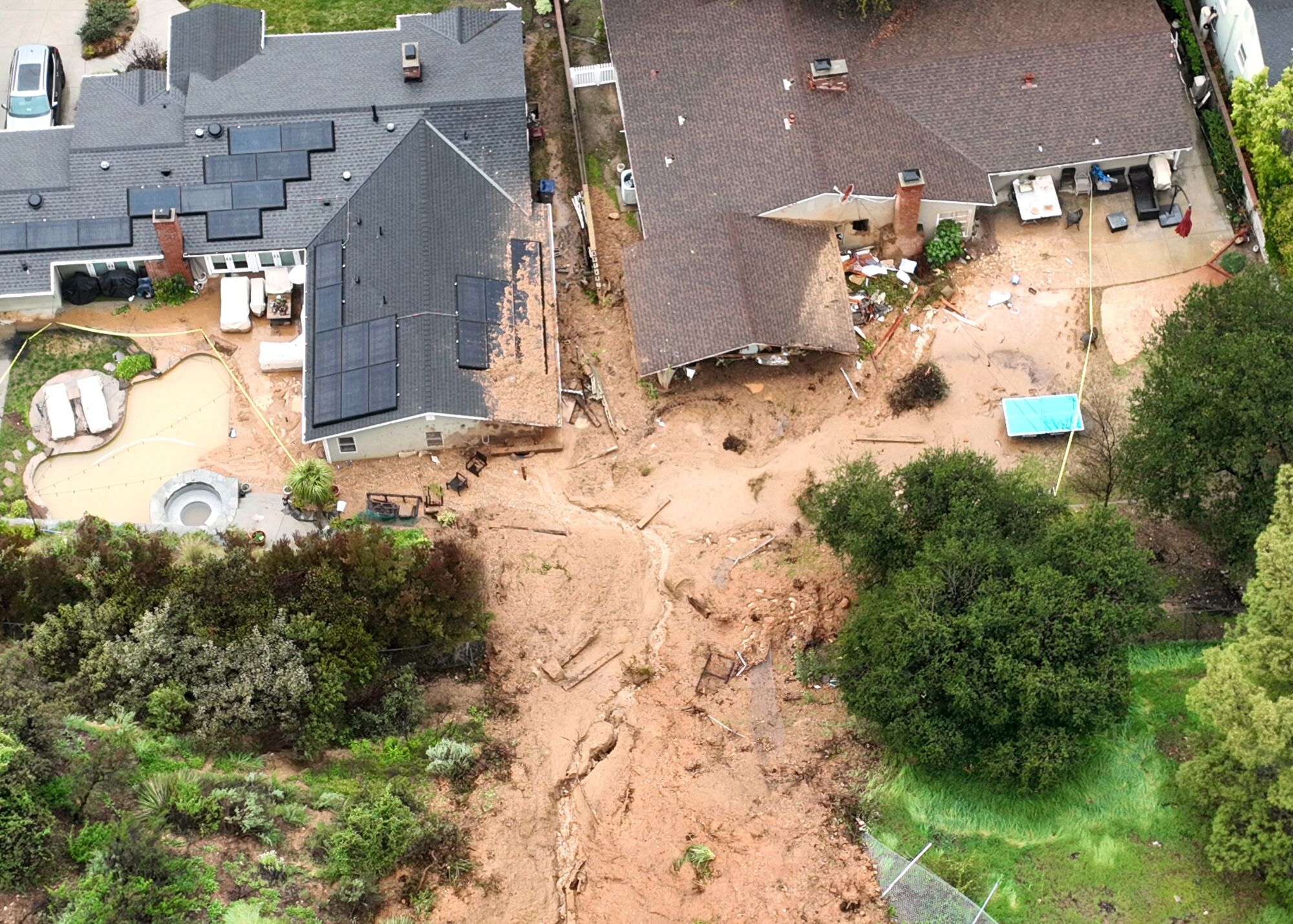 An aerial view of a mudslide running down the middle of the frame toward two one-story homes; damaging and breaking one.