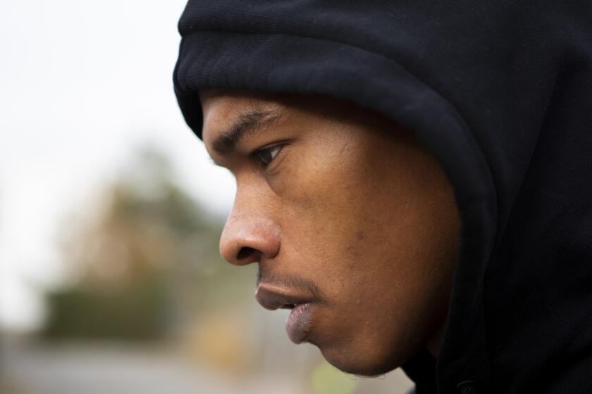 A profile view of rapper Lil Baby's face with his head covered by a black hoodie