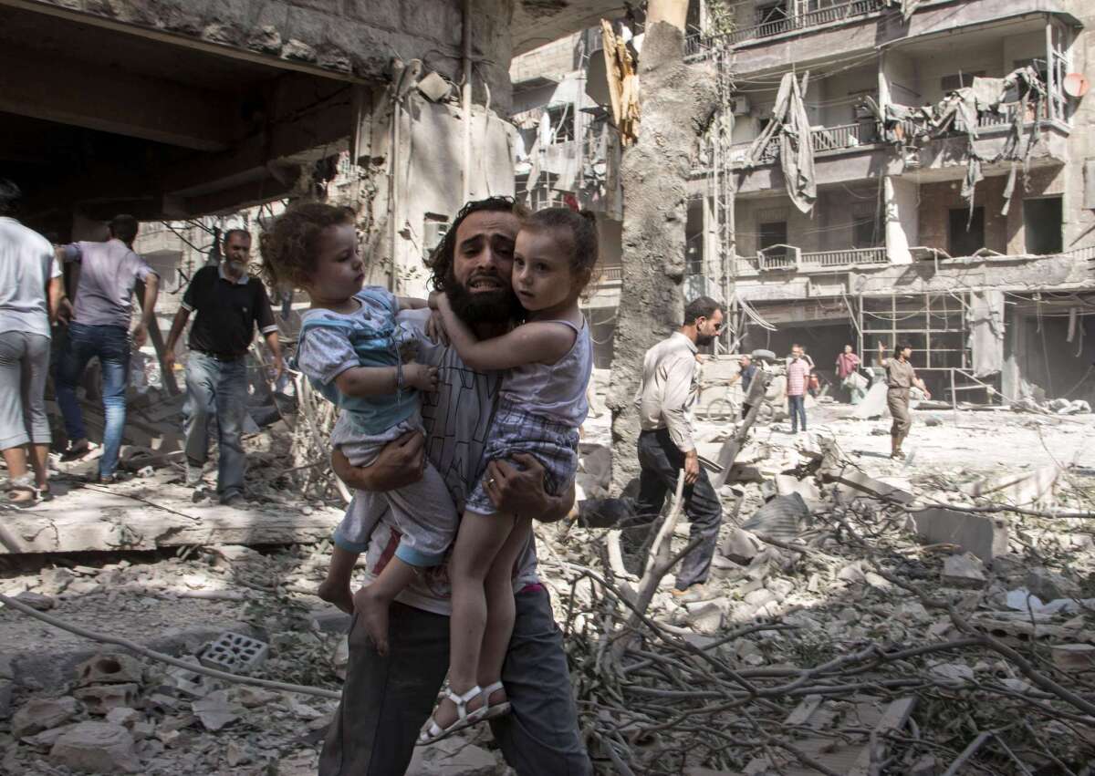 A Syrian man carries his two girls as he walks across the rubble following a barrel bomb attack on the rebel-held position in the northern Syrian city of Aleppo.