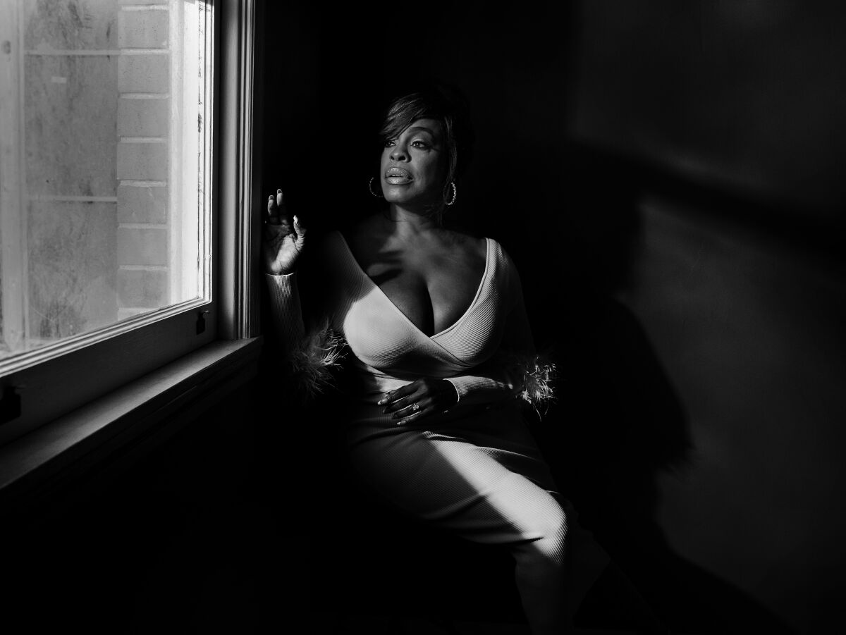 Niecy Nash-Betts looks out the window she is sitting next to for a black-and-white portrait.
