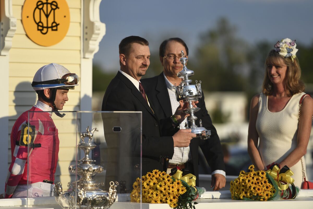 Rombauer trainer Michael McCarthy holds the trophy as others look on after winning the Preakness Stakes horse race.