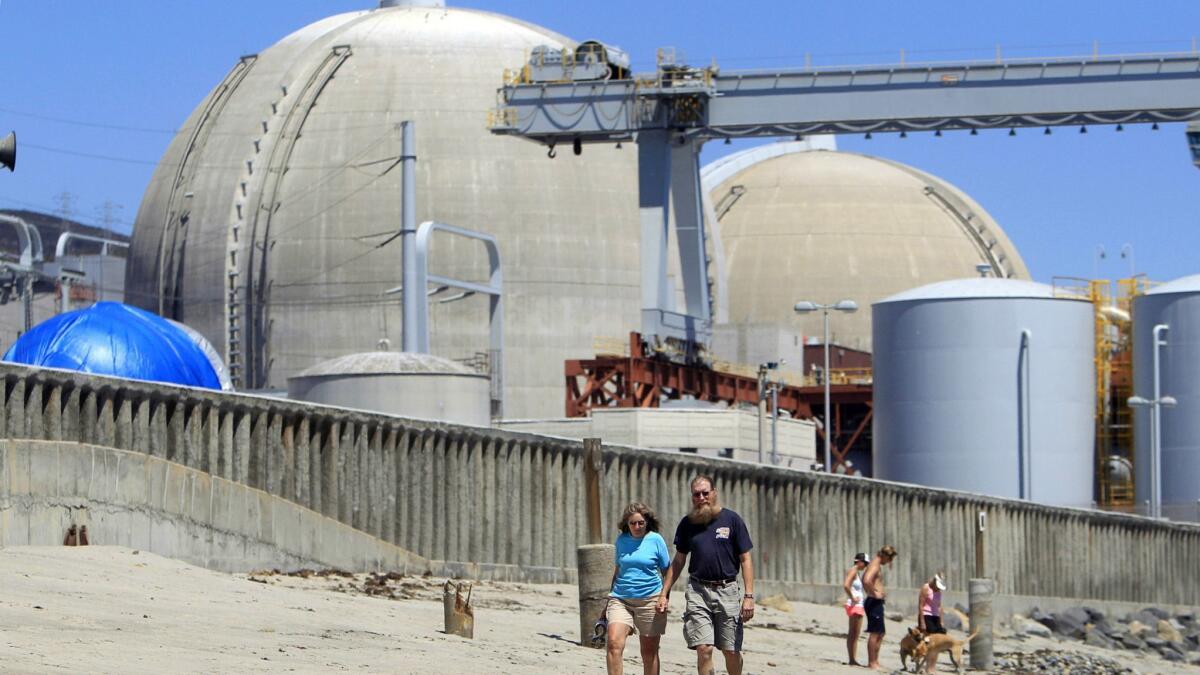 People walk on the sand near the shuttered San Onofre nuclear power plant near San Clemente in 2011.