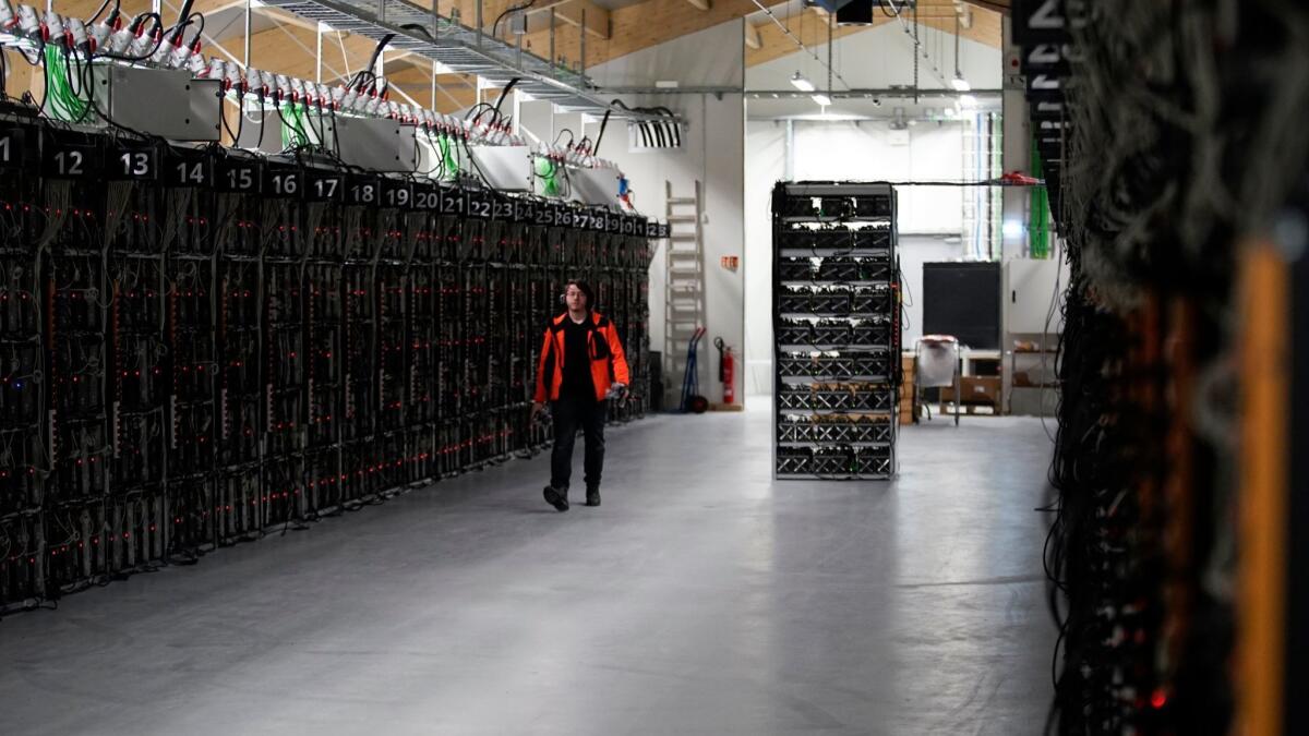 A worker walks along a row of computer rigs that run around the clock "mining" bitcoin inside the Genesis Mining cryptocurrency mine in Keflavik, Iceland.