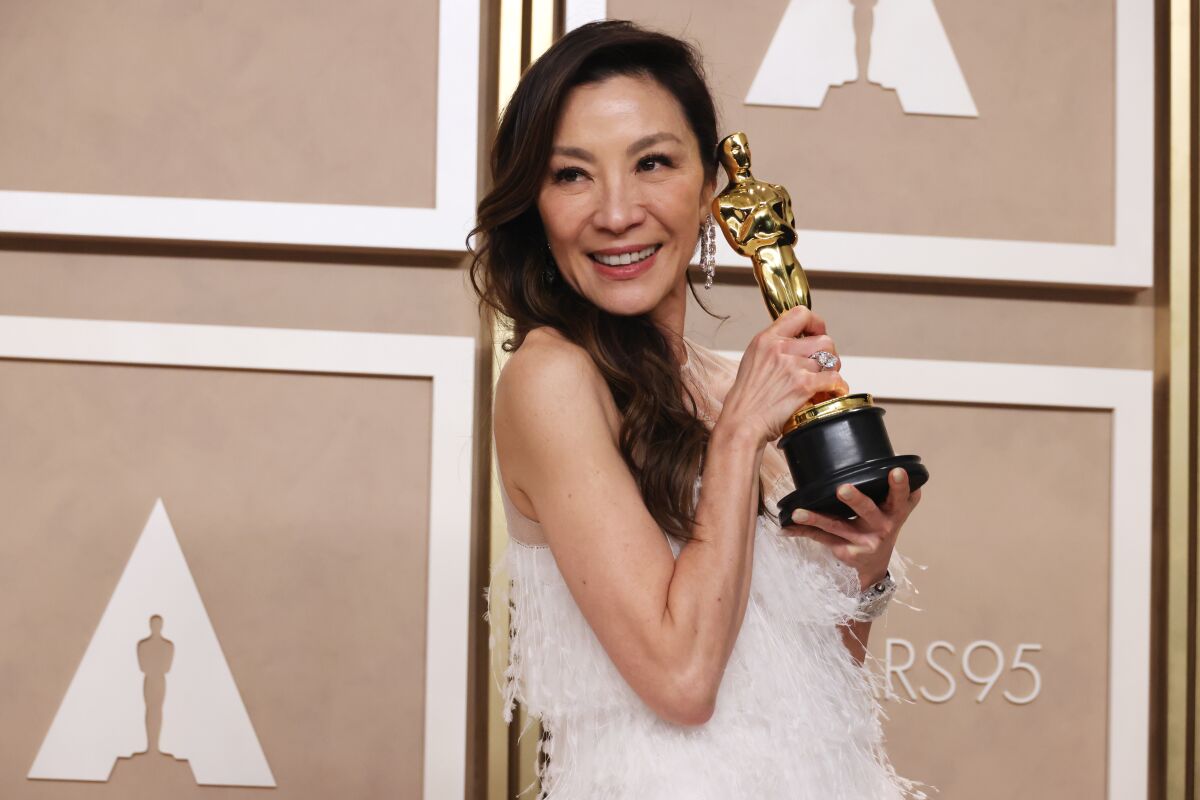 A woman in a white dress poses with an Academy Award statuette.