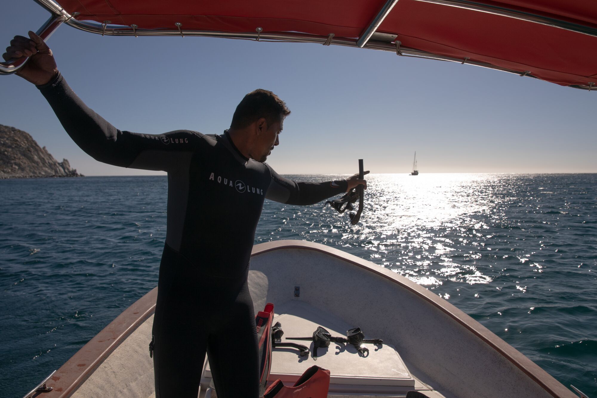 A man in scuba gear on a boat, pointing out over the watery horizon.