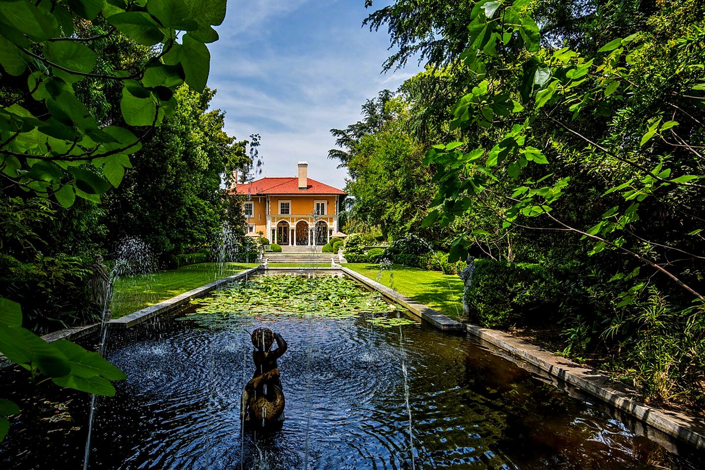 A loggia lines the home’s backside, descending to a swimming pool and grassy lawn. Manicured gardens, lily ponds and a tennis court fill out the rest of the 2.4-acre grounds.