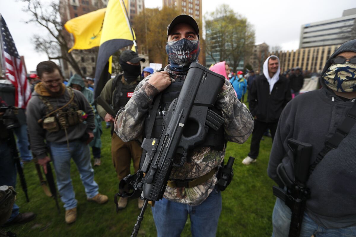 A protester carries his rifle outside the State Capitol in Lansing, Mich., while other armed people stand around him.