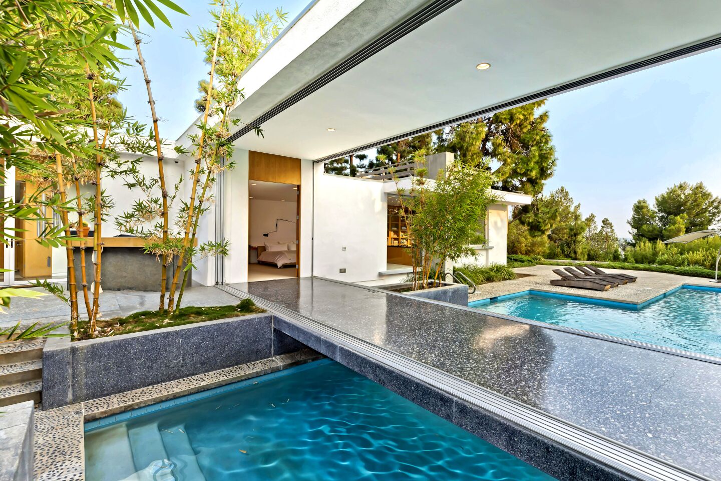 This custom Midcentury revolves around indoor-outdoor living with a series of rooms surrounding a courtyard and a bridge over the swimming pool that runs from the owner's suite to the living room.