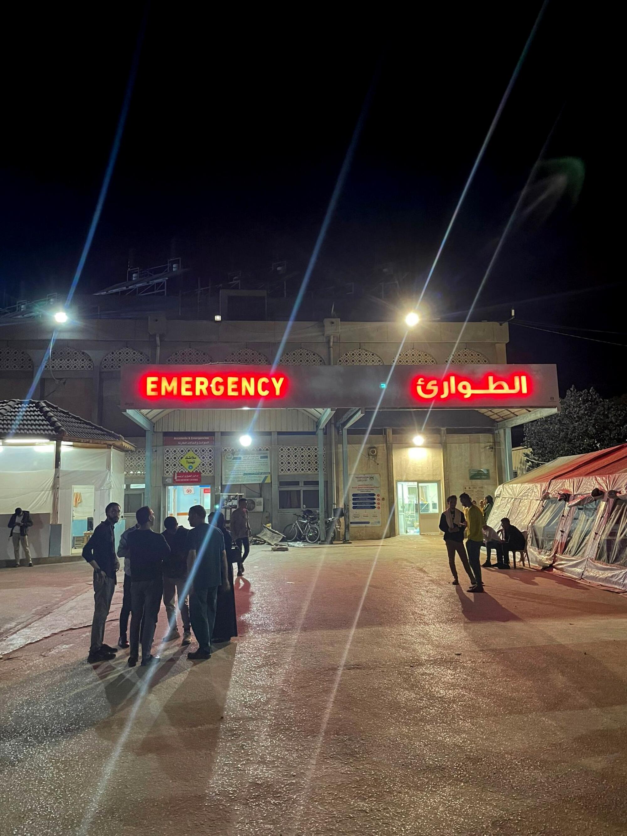 Groups of people stand outside the entrance to a hospital emergency department.