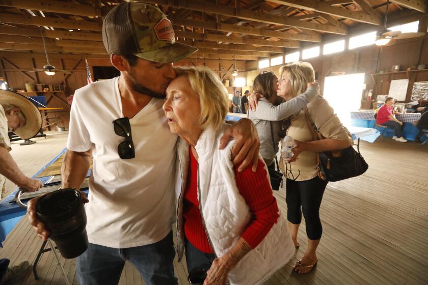 BAKERSFIELD, CA - OCTOBER 19, 2019 - - Pat Rush, 84, gets a kiss of support from her grandson Gabriel Wood, in one of the structures that shares historic photos and memorabilia at the Weedpatch Camp in Bakersfield on October 19, 2019. Rush and her family lived in the migrant camp after migrating from Oklahoma to Bakersfield in 1945. After three decades, the Dust Bowl Days festival at Sunset Labor Camp, which housed Okies and migrant workers during the Dust Bowl, is ending its run. The final festival celebrates Okie history. (Genaro Molina / Los Angeles Times)