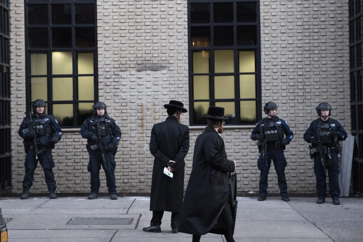 Orthodox Jewish men pass New York  police guarding a Brooklyn synagogue on Dec. 11.