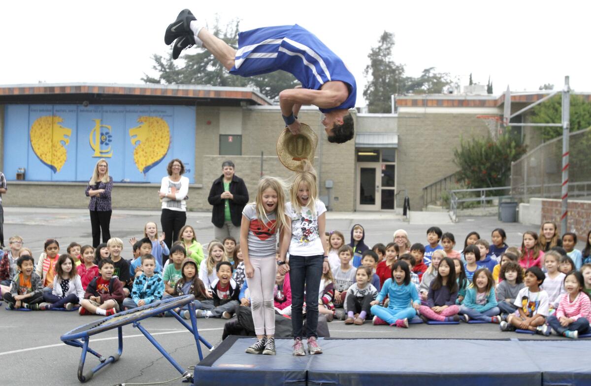 Keith Cousino of the TNT Dunk Squad flips as he grabs a hat off of student Katherine O'Callahghan during dunking demostration at La Canada Elementary School's playground in La Canada Flintridge on Tuesday, March 25, 2014. Grace Frame at center left also had her hat removed by another dunker.