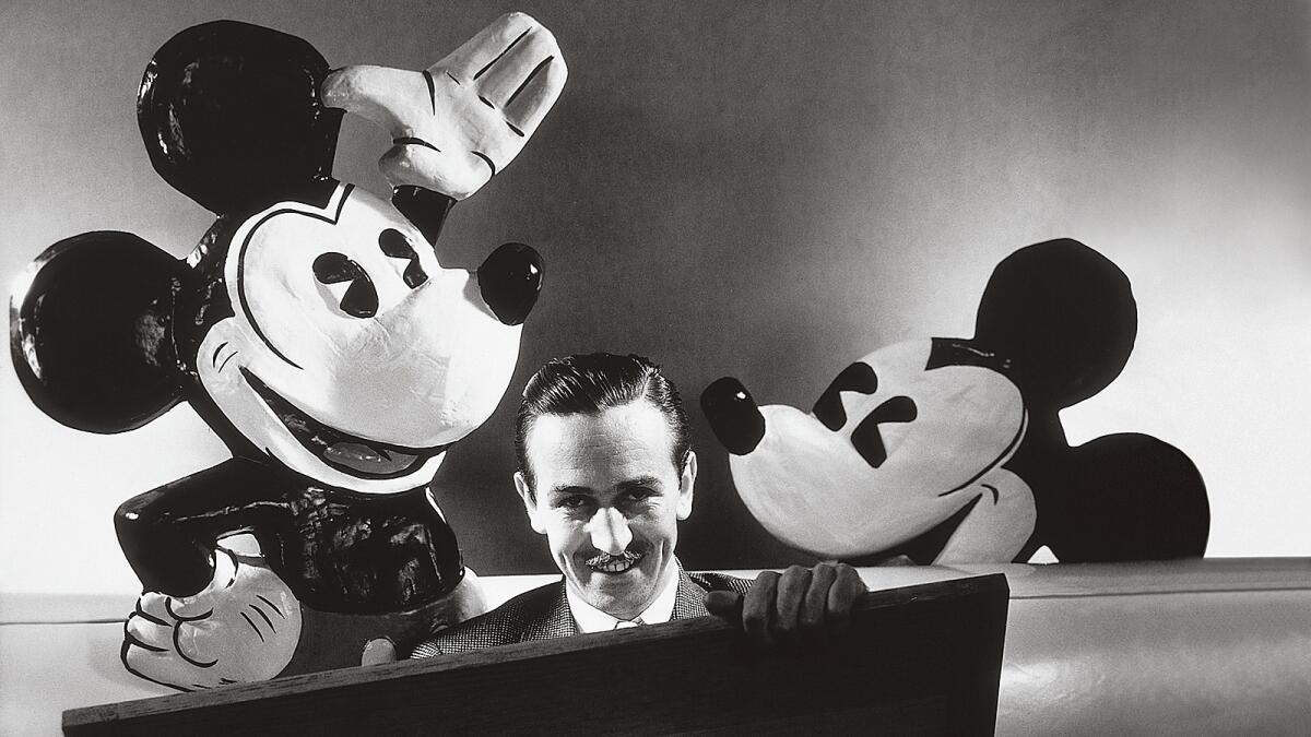 Walt Disney is seated with a drawing board on his lap and representations of his creations Mickey and Minnie Mouse behind him in October 1933.