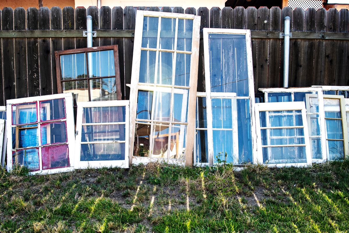Wood-frame windows lean against a fence.