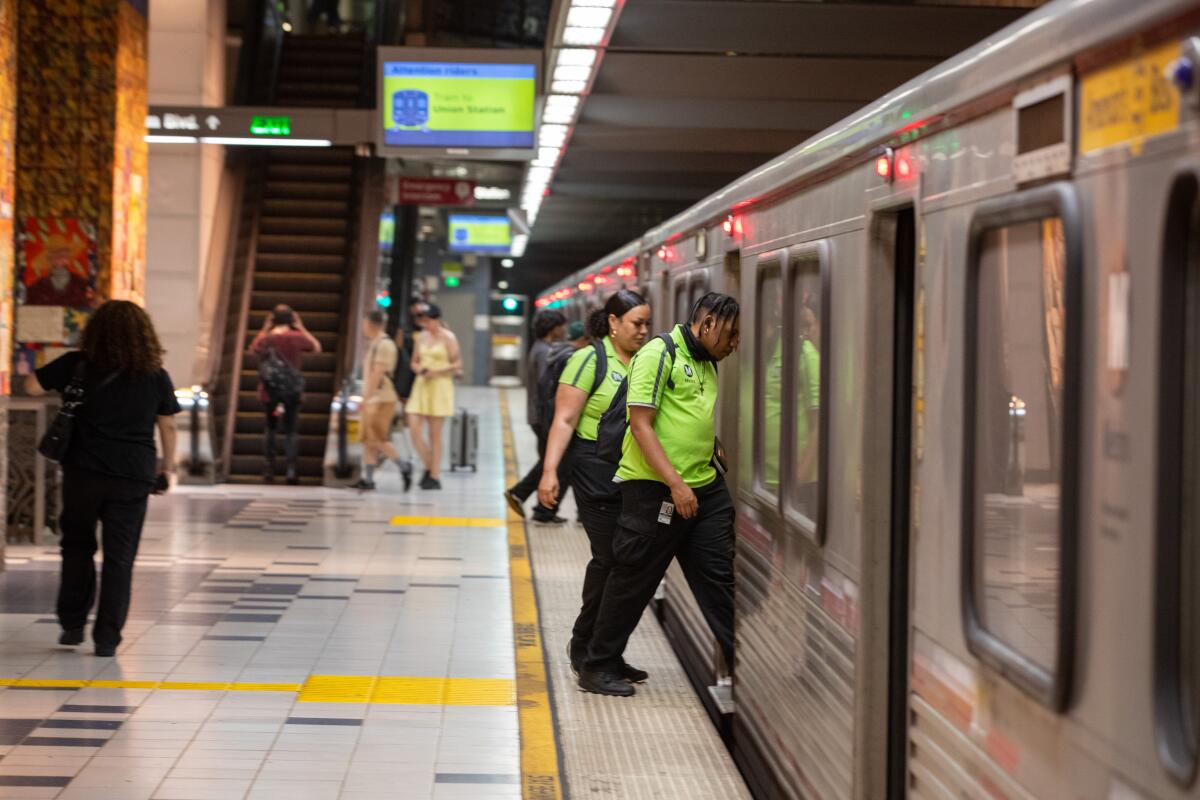 Two green-shirted Metro workers board a train