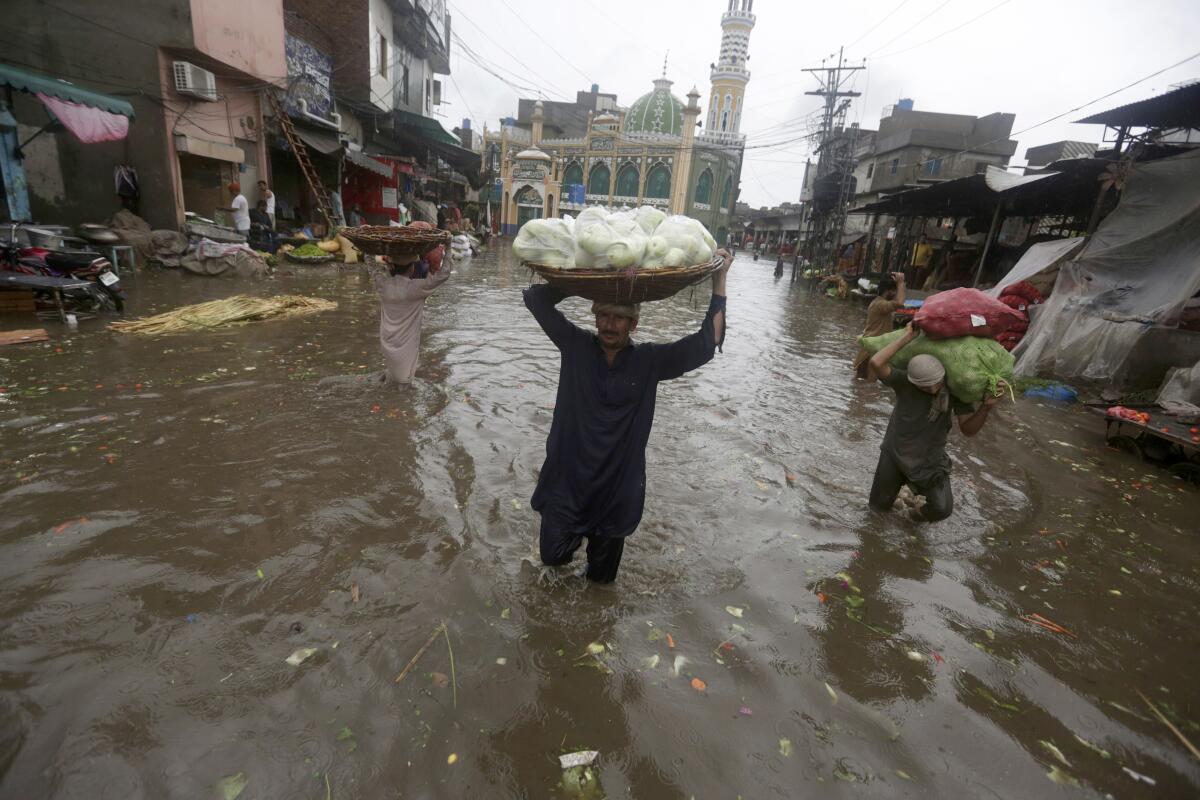 Laborers carry produce as they wade through a flooded road after heavy rainfall, in Lahore, Pakistan, Thursday, July 21, 2022. (AP Photo/K.M. Chaudary)