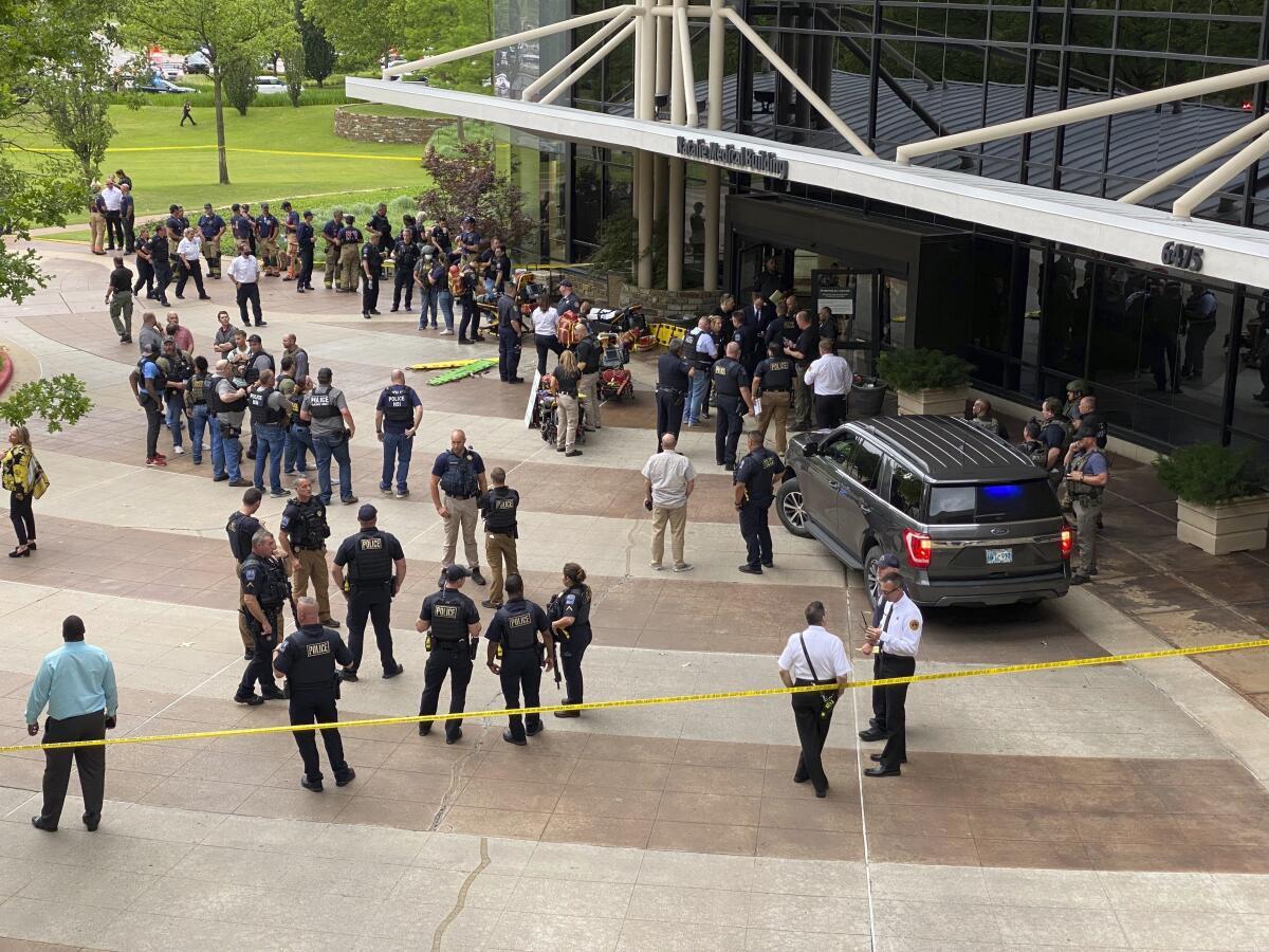 Law enforcement personnel gather inside caution tape outside a building.