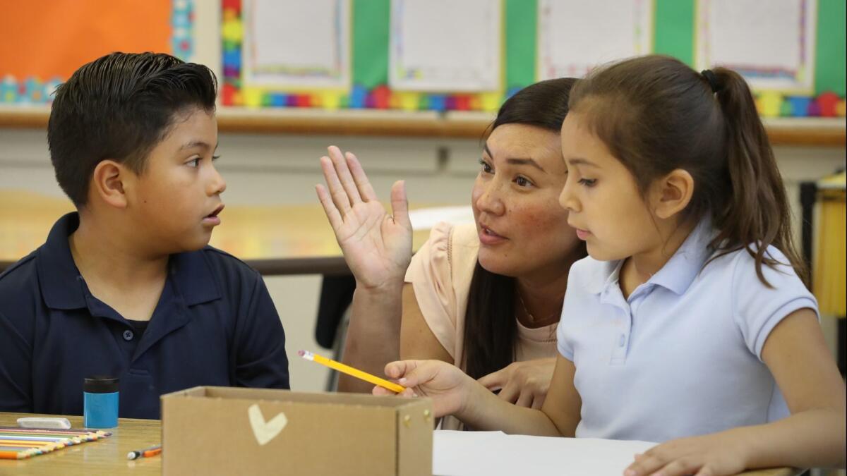 Teacher Roxana Okamoto helps second-graders Damian Cortez, left, and Melody Camarena in a lesson about hurricanes at Sunrise Elementary, which is competing for students with a charter school on the same campus.