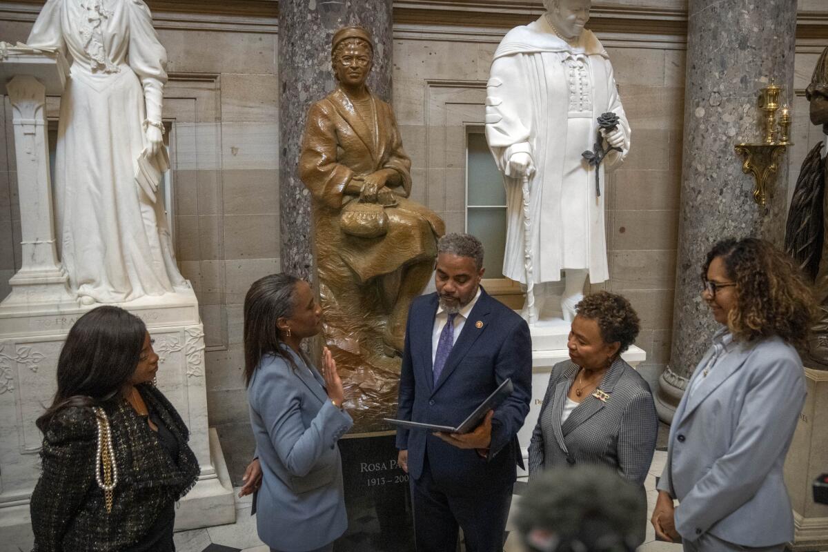 Laphonza Butler raises her right hand for a swearing-in next to a gold statue of Rosa Parks as fellow Black lawmakers look on
