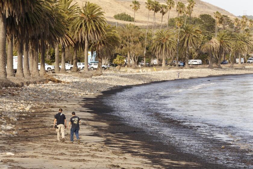 Diego Topete, left and Ryan Cullom walk May 19 on the oil-coated Refugio State Beach.