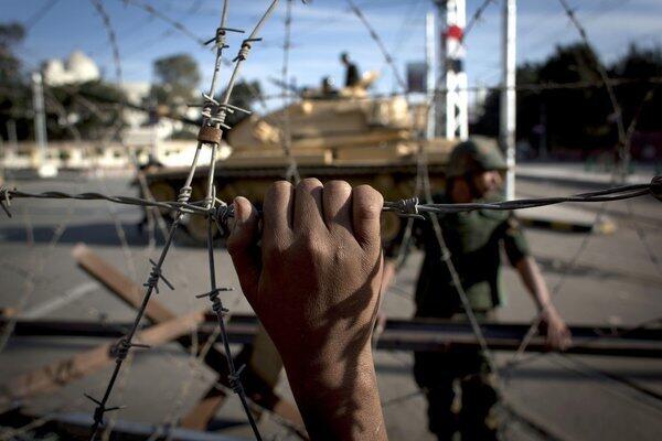 An Egyptian army tank is seen behind barbed wire securing the perimeter of the presidential palace in Cairo while protesters on the other side chant anti-President Mohammed Morsi slogans.