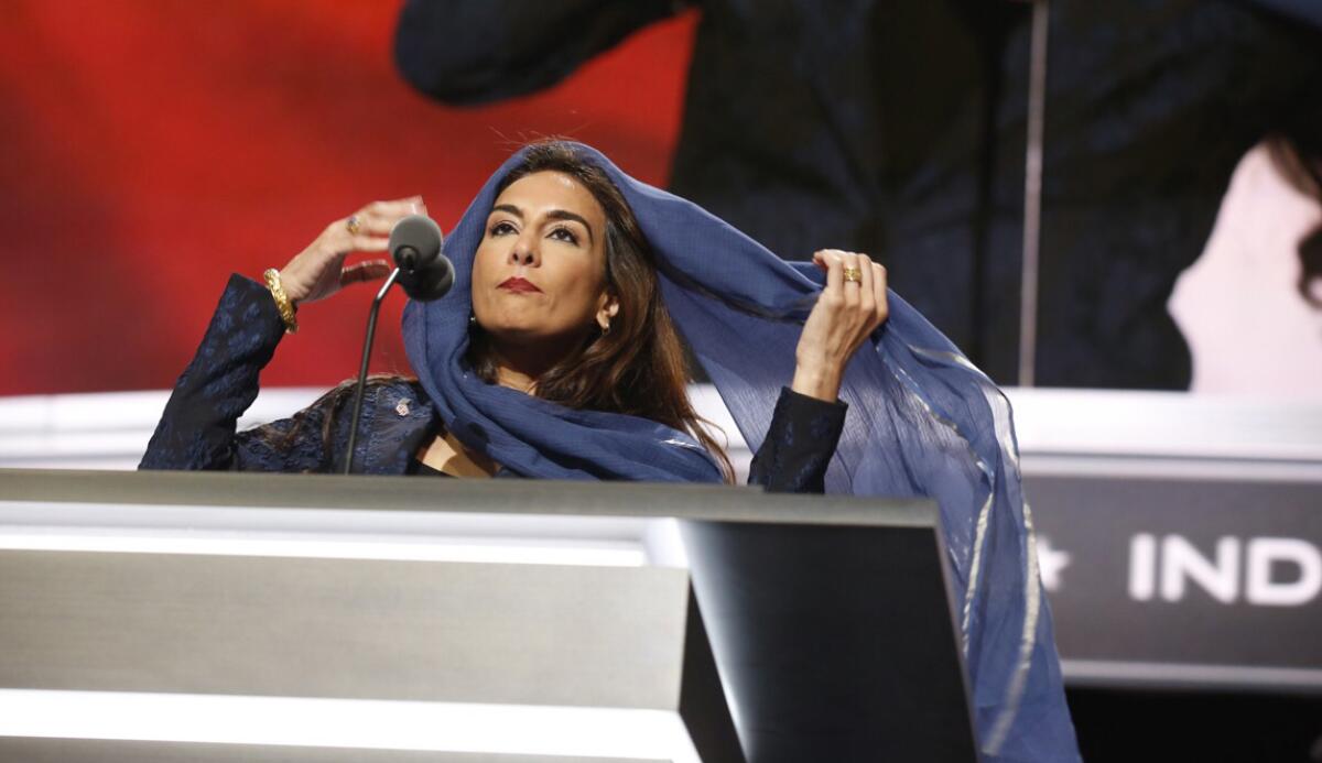 A woman covers her hair at a podium