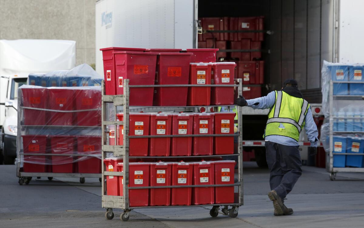 A worker at Stericycle pulls a cart stacked with containers of biohazardous waste.