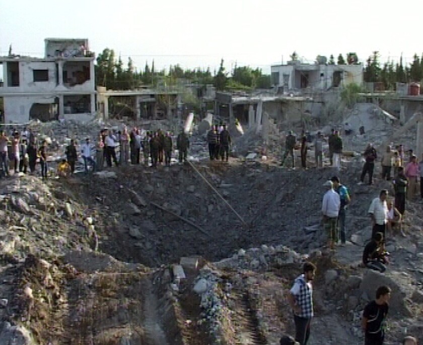 A photo released by the official Syrian Arab News Agency reportedly shows people gathering around a crater after a massive car bomb attack Friday in the village of Hurra outside the central city of Hama.