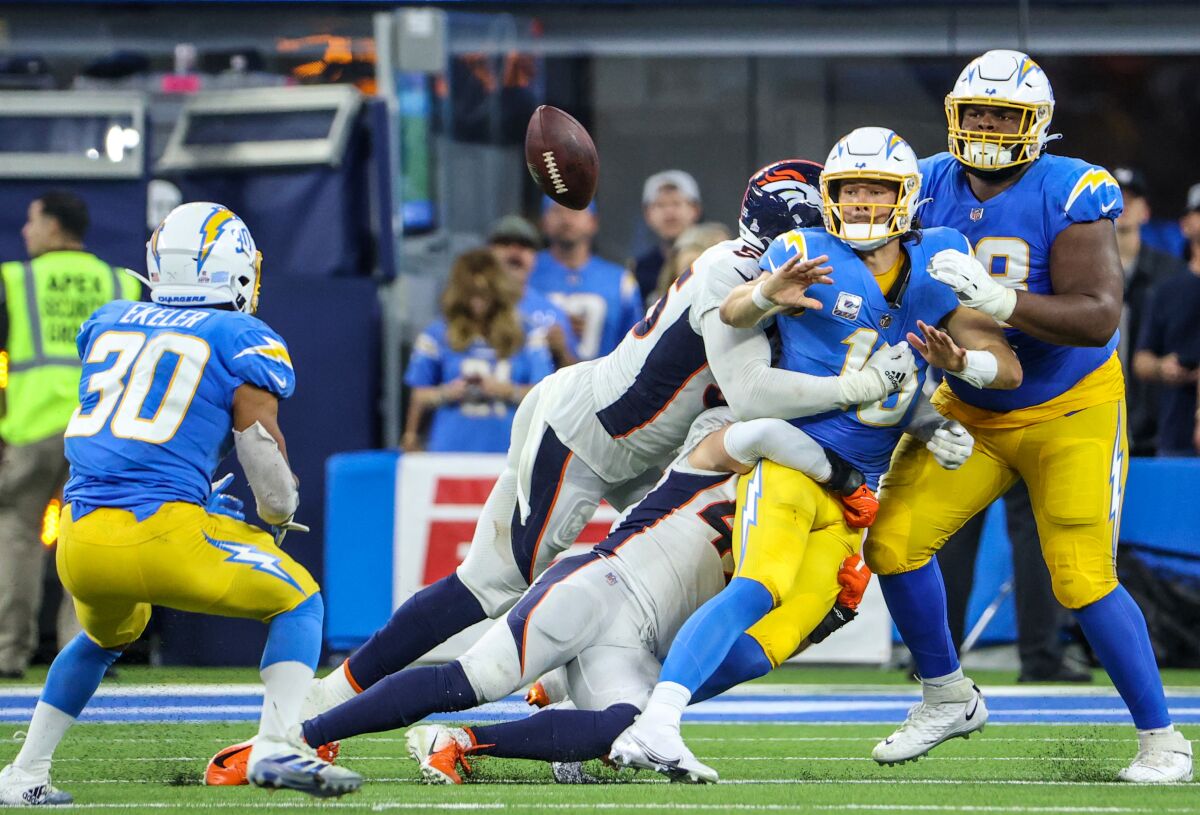 The Chargers' Justin Herbert (10) turns a pass to Austin Ekeler (30) when he is tackled late in the game against the Broncos.