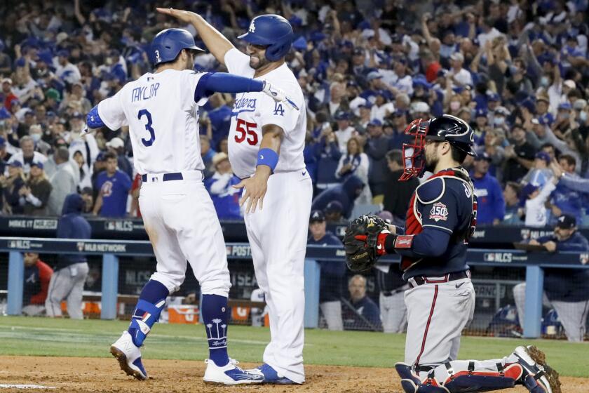 Los Angeles, CA - October 21: Los Angeles Dodgers' Chris Taylor, from left, hugs Albert Pujols after a two-run home run in the fifth inning in game five in the 2021 National League Championship Series as Atlanta Braves catcher Travis d'Arnaud looks on at Dodger Stadium on Thursday, Oct. 21, 2021 in Los Angeles, CA. (Robert Gauthier / Los Angeles Times)
