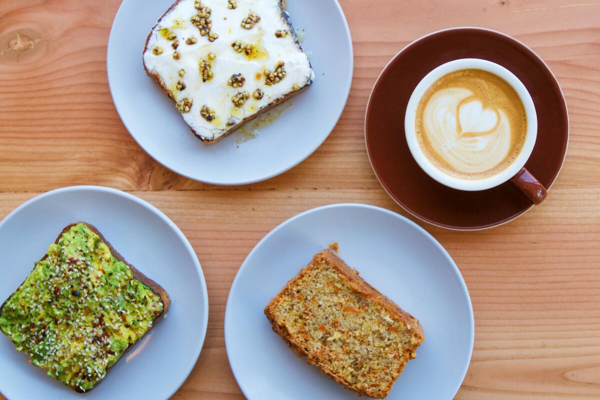 An overhead photo of a Canyon Coffee latte with avocado toast, labneh toast, and a slice of coconut carrot loaf.
