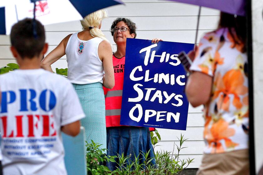 A volunteer at Causeway Medical Clinic in Metairie, La., stands at the entrance July 23 with a sign as antiabortion activists protest outside.