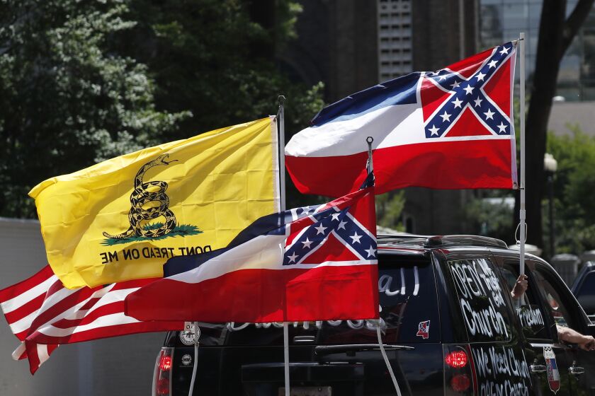 In this April 25, 2020 photo, Mississippi state flags are positioned on a vehicle amid an arrangement with the American flag and a Gadsden flag during a drive-by "re-open Mississippi" protest past the Governor's Mansion, in Jackson, Miss. There is a growing movement to replace the current state flag that has in the canton portion of the flag the design of the Civil War-era Confederate battle flag. (AP Photo/Rogelio V. Solis)