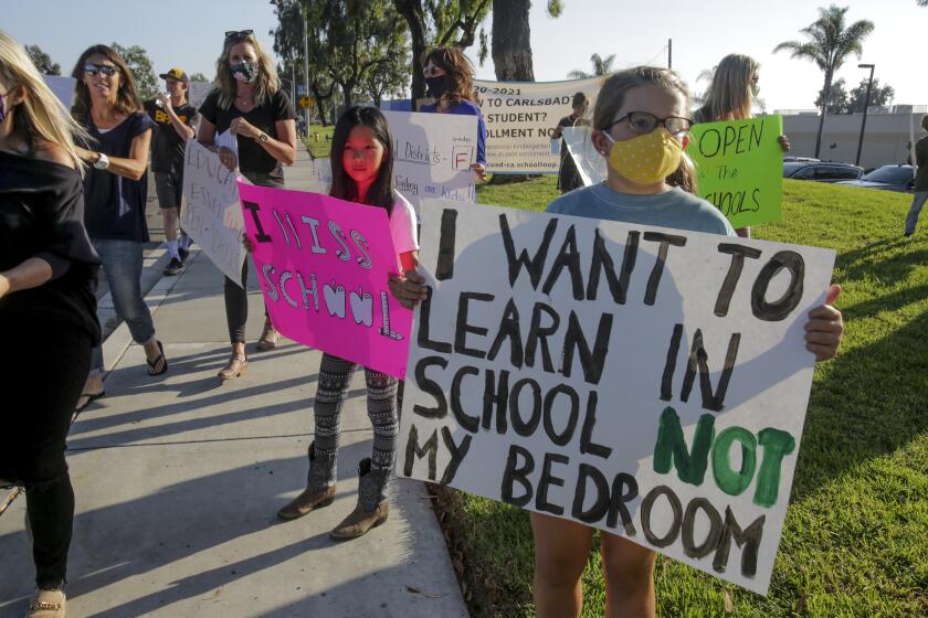 Morgan Yang, 9, center, and Lucy Riddle, 10, display signs urging officials to open schools during a protest Wednesday, 09/23/2020, in front of the Carlsbad School district headquarters calling for schools in Carslbad to open. photo by Bill Wechter