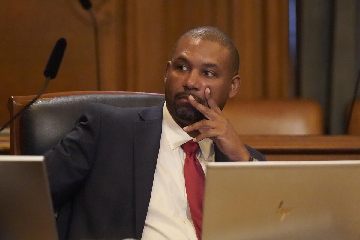 Supervisor Shamann Walton looks to the left while holding some of his fingers up to his face while seated.