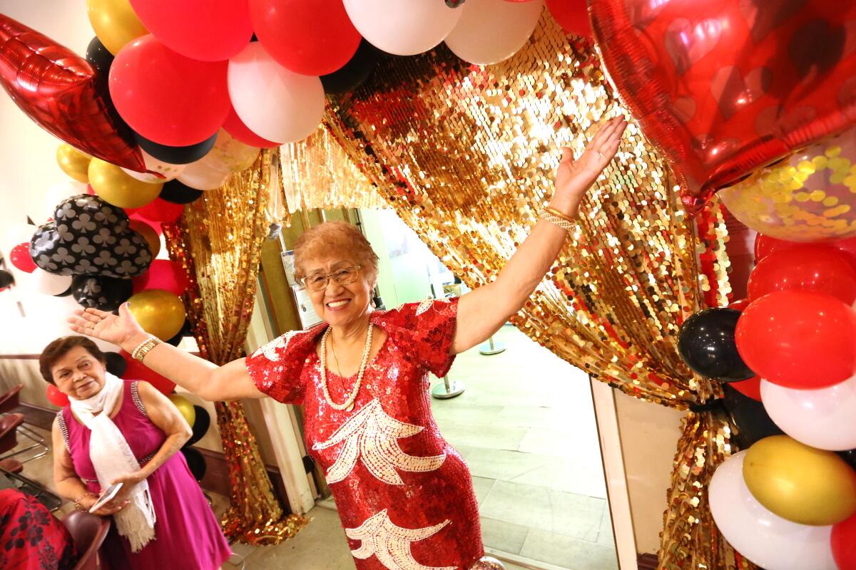 A woman in a red dress stands with arms held high under a balloon arch.