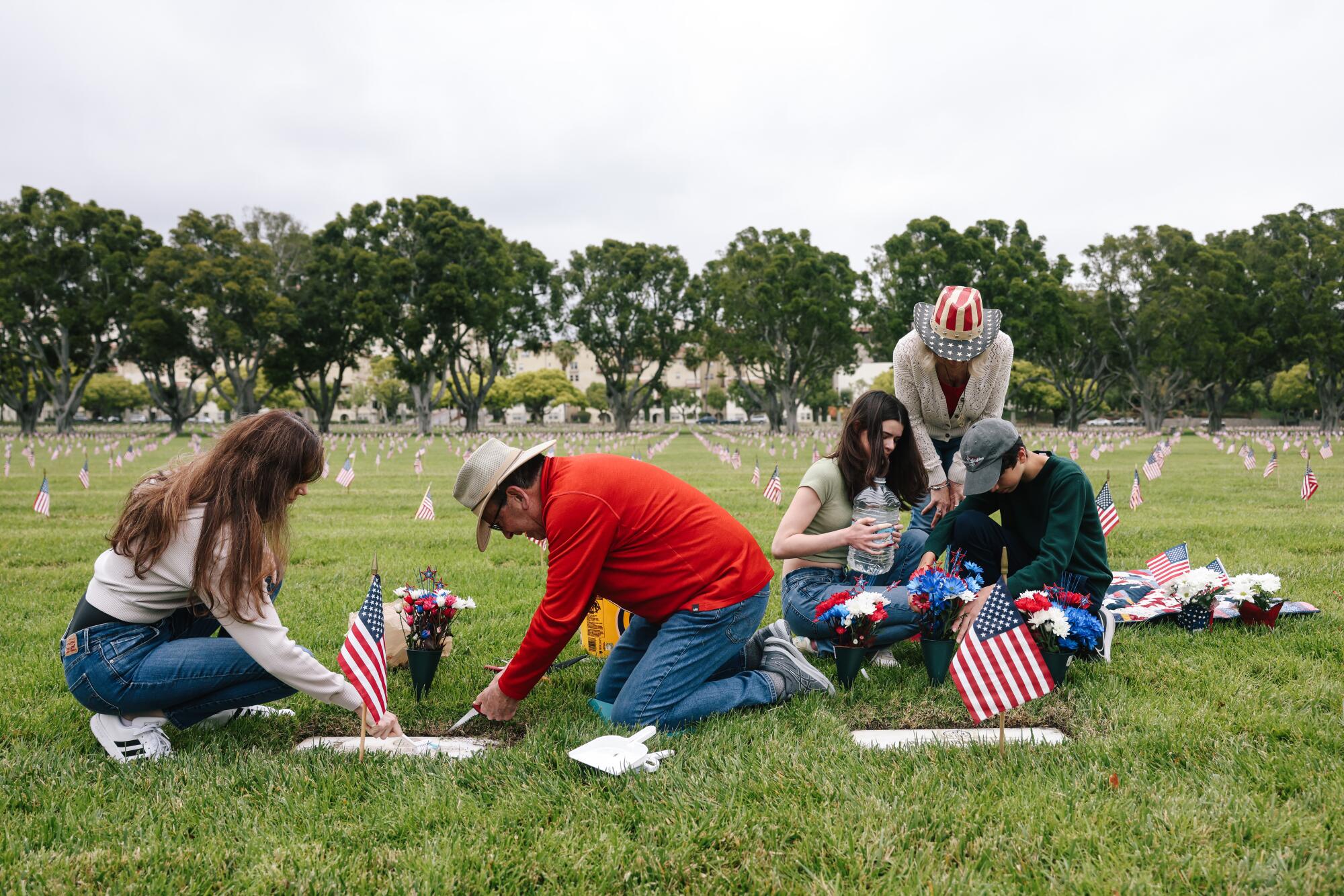 Quatro pessoas em um cemitério se ajoelham e limpam sepulturas.