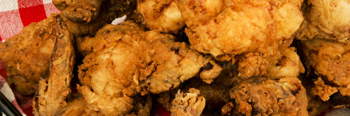 Crispy fried chicken is piled into a basket lined with a red and white checked napkin.