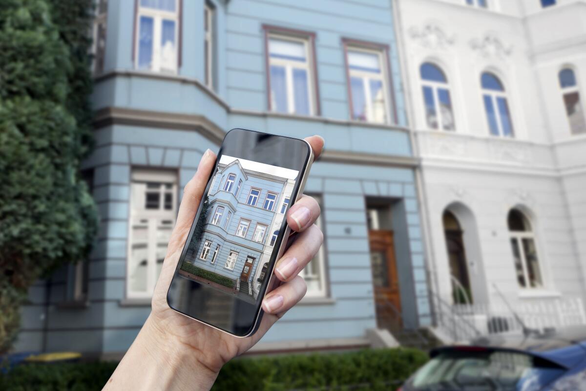 A person holding an iPhone taking a photo of a house