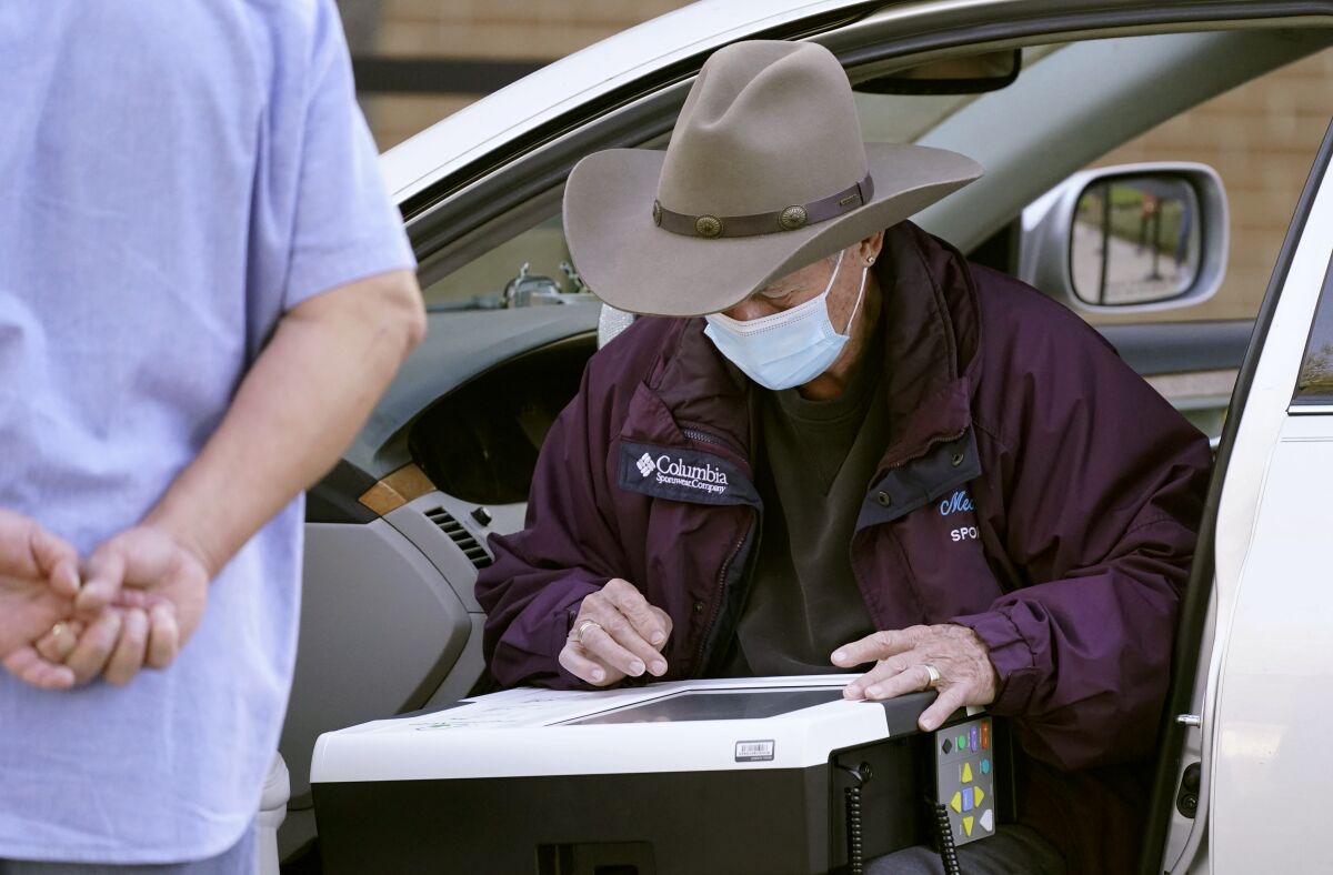 With an election official looking on an elderly voter uses the drive-thru option to vote outside Richardson City Hall during early voting Tuesday, Oct. 13, 2020, in Richardson, Texas. (AP Photo/LM Otero)