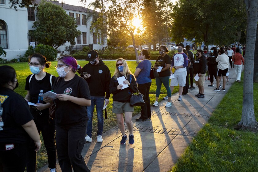 People wearing masks stand in a long line on sidewalk outside a community center